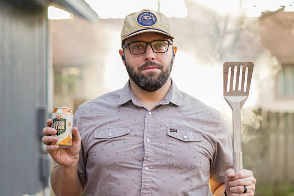 Man after cleaning his BBQ grill holding a grill spatula and a can of beer.