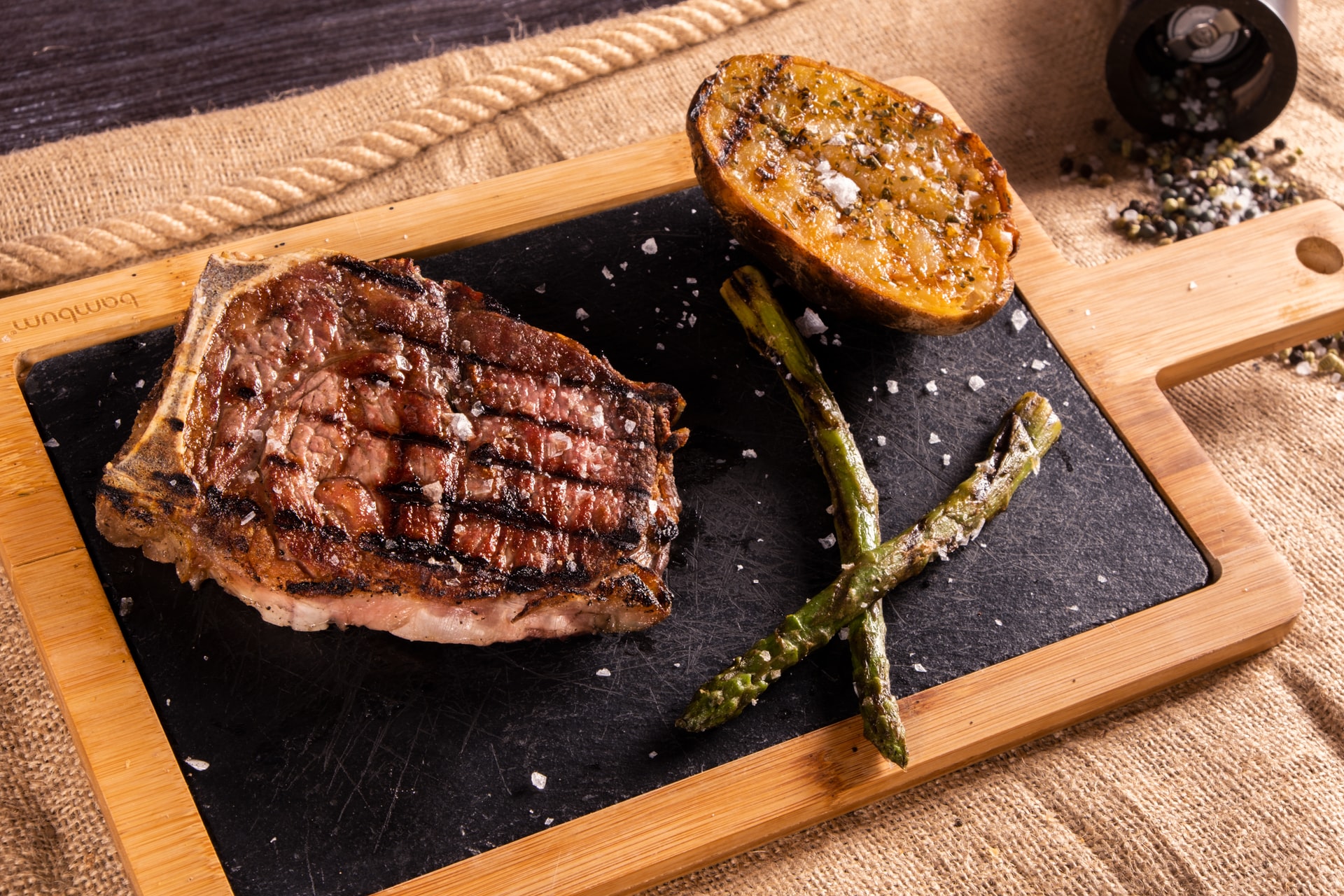 Grilled charred steak resting on a board with asparagus and a potato