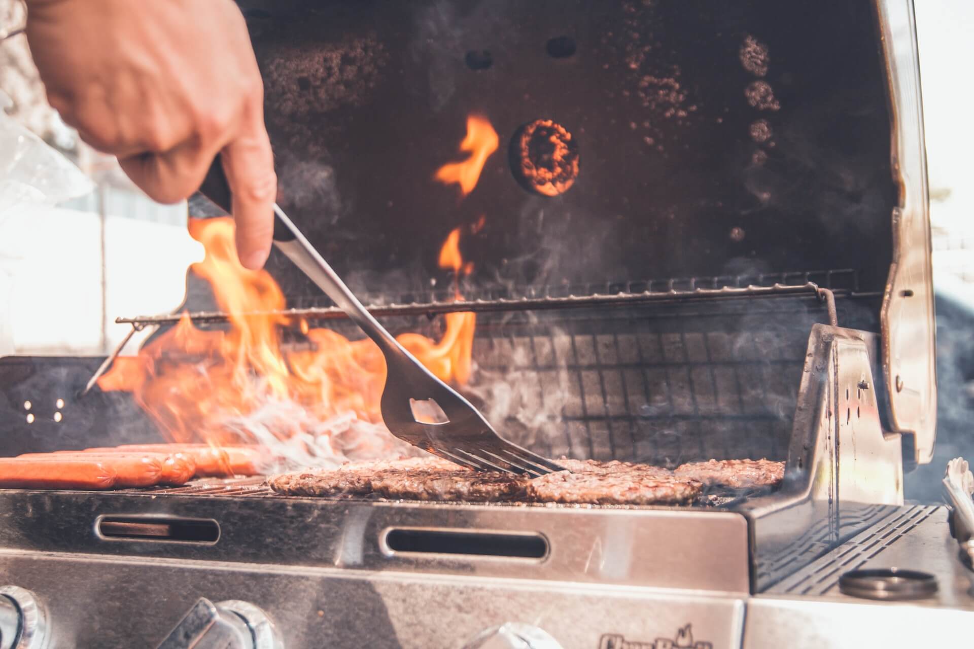 A person is cooking burgers and hot dogs on an outdoor gas grill