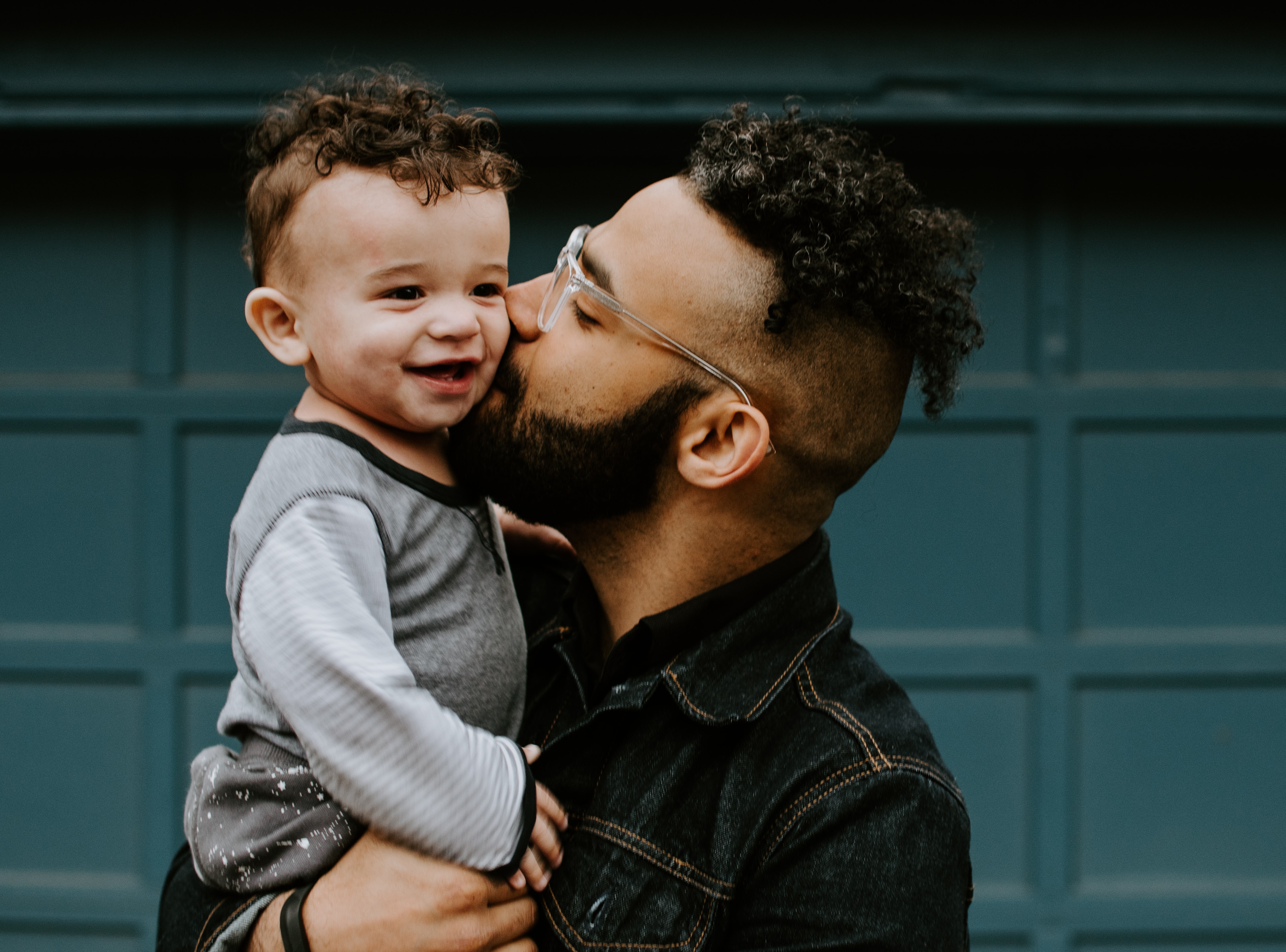 Father and child with matching haircuts embracing in front of a garage