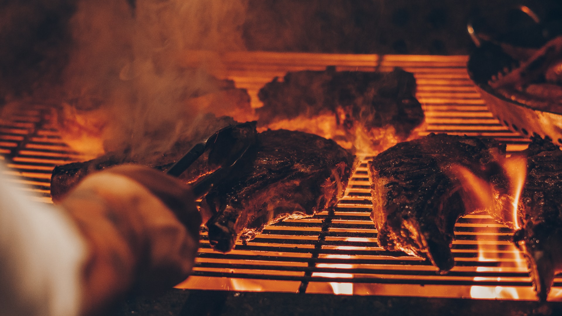 Someone turning steaks on a grill