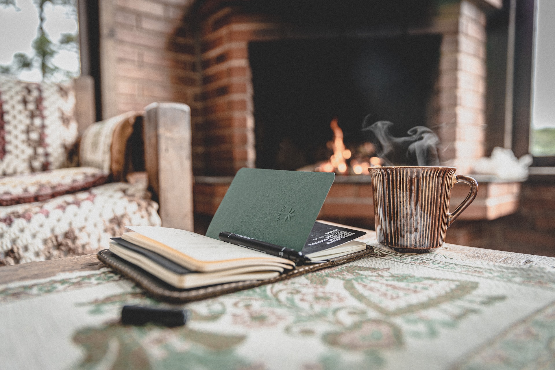 Journal and steaming drink with a fireplace in the background